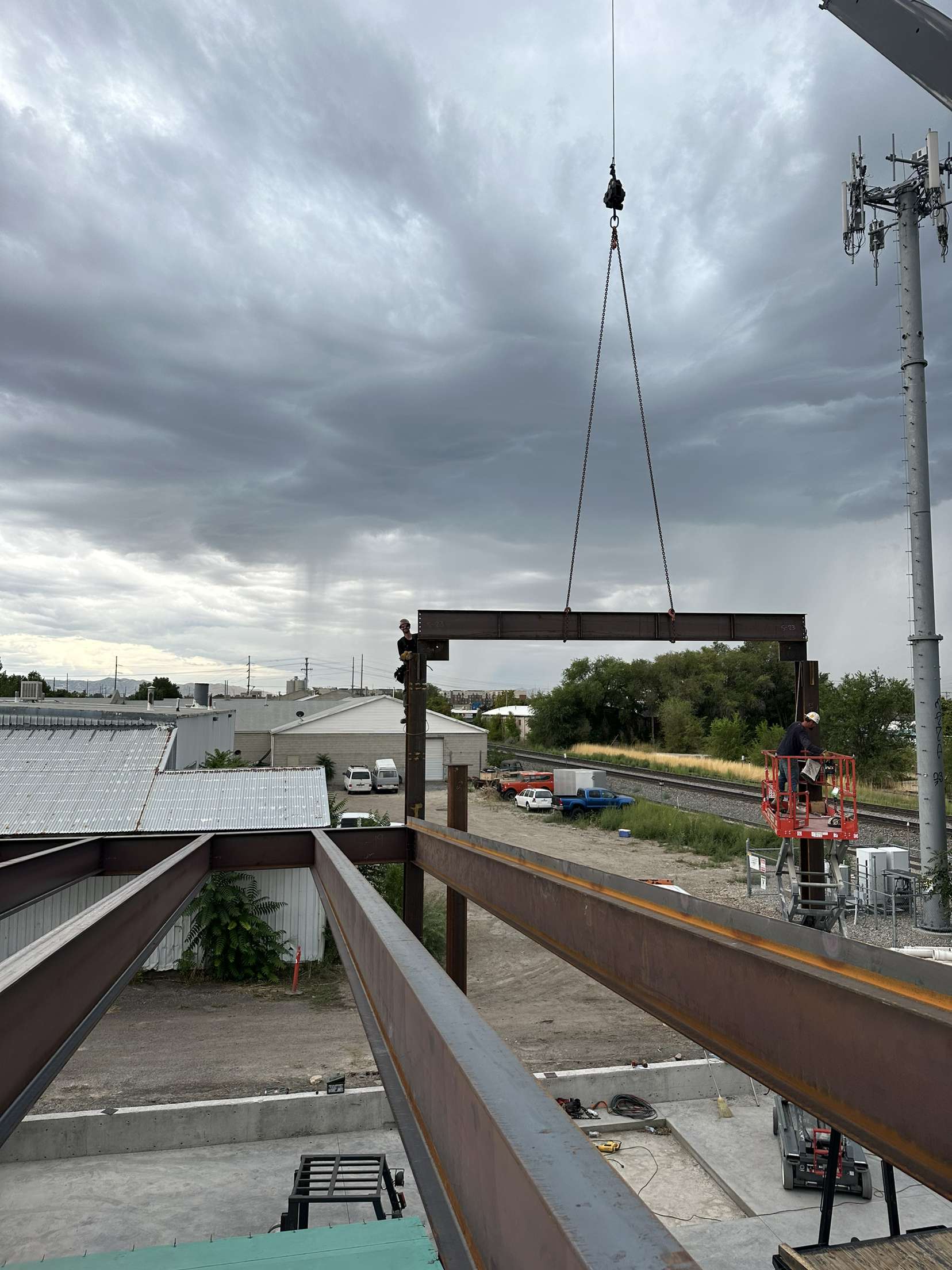 Crane lifting a structural steel beam between columns during field erection