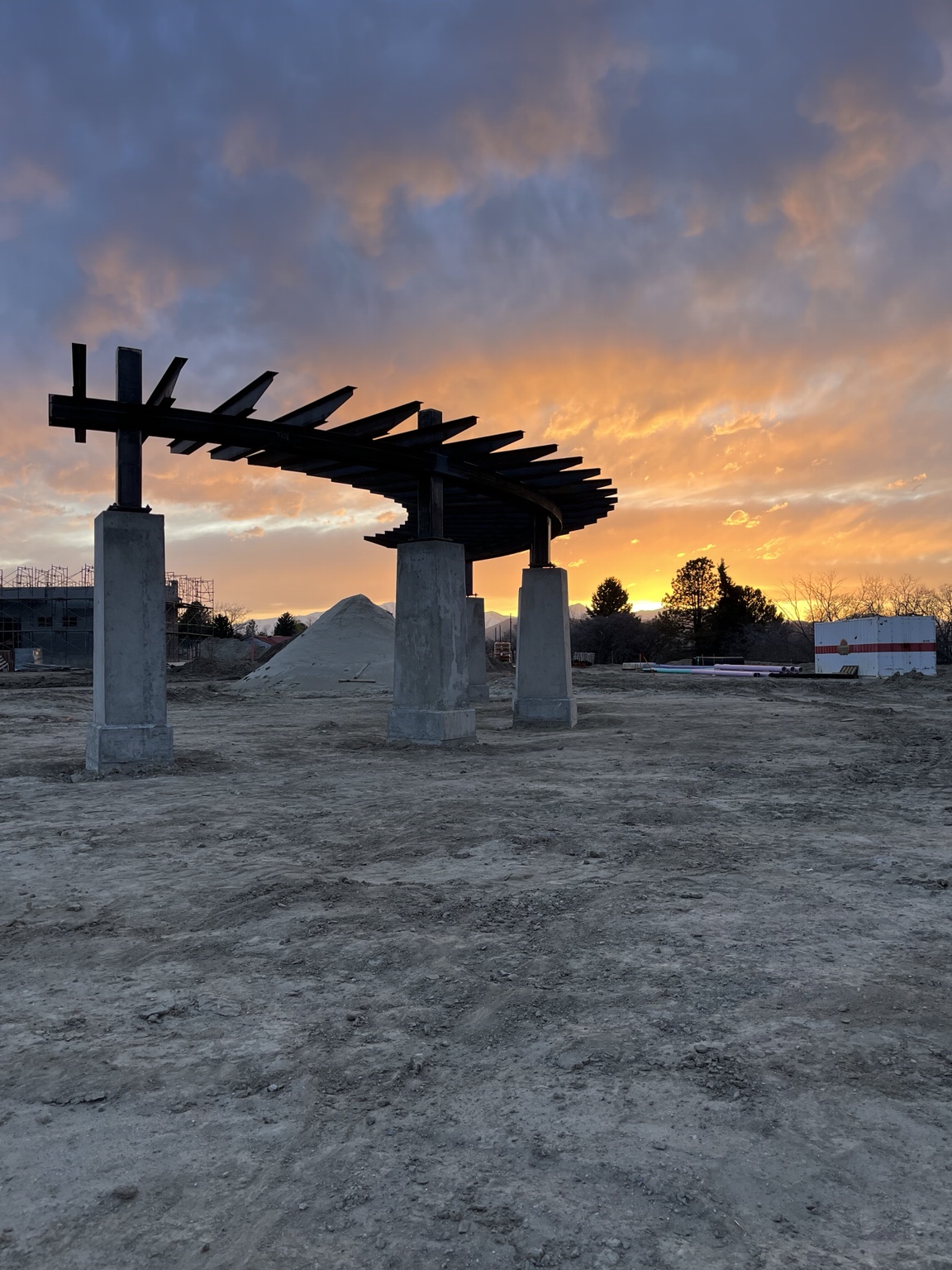 Curved structural steel framing on concrete columns at sunset
