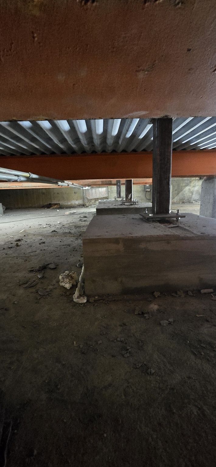 Steel columns anchored to concrete bases beneath beams and metal decking