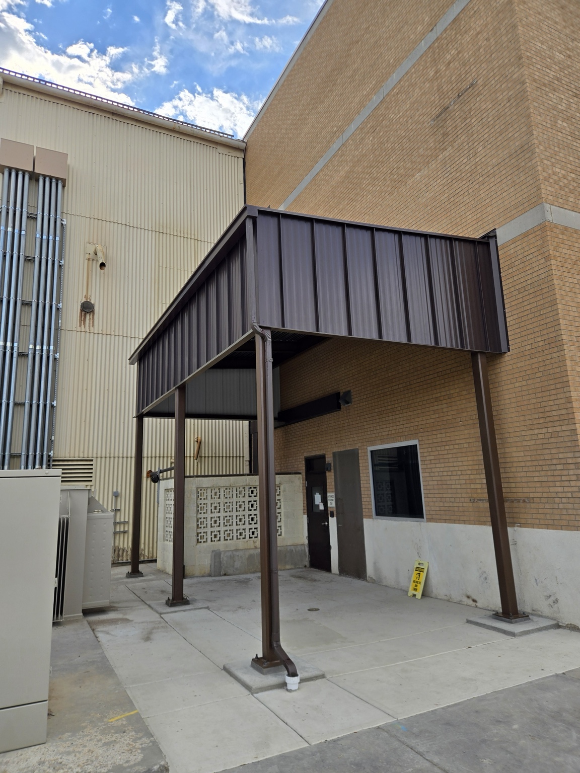 Steel entry canopy with metal roof panels beside a brick building